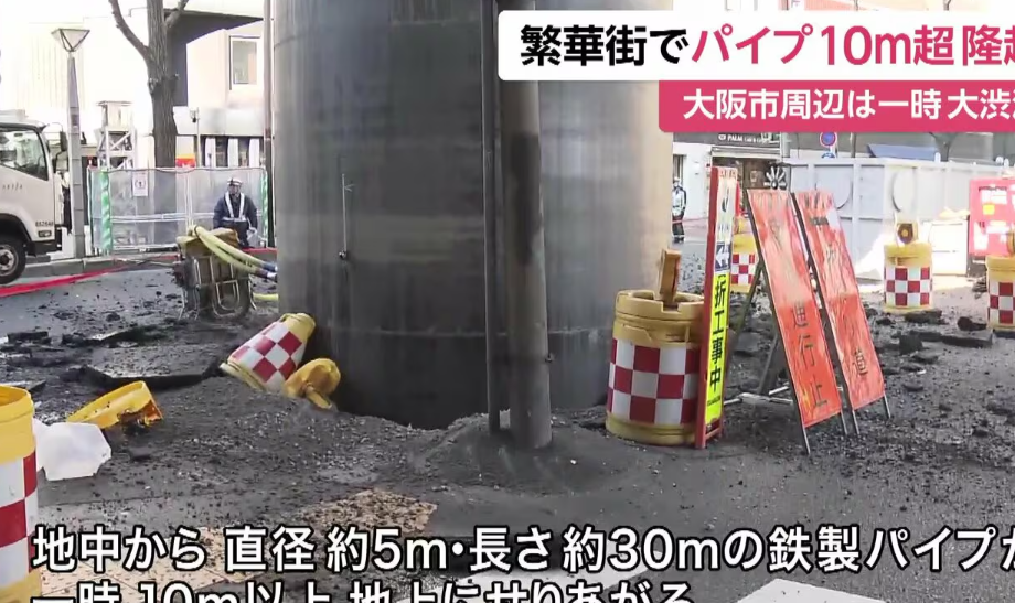 日本JR大阪站附近馬路一條深埋地下長約30米、直徑約5米的大型水管突「破土而出」無故隆起18米。(影片截圖)