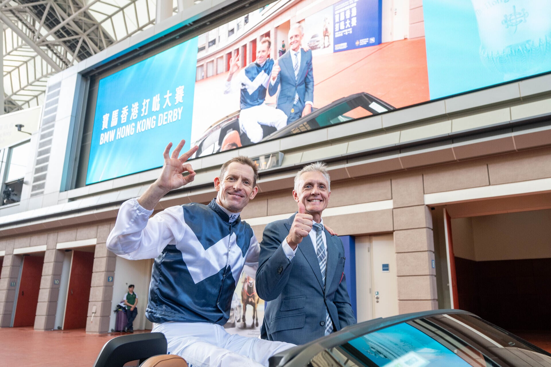 「白鷺金剛」的騎師布文(左)及廖康銘(右)賽後乘坐開篷跑車在馬匹亮相圈上巡遊,接受馬迷祝賀。(馬會圖片)