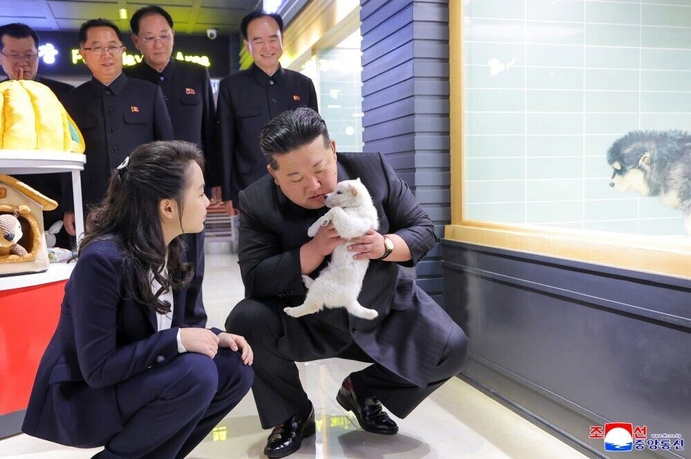 金正恩抱著白色小狗,身後官員露出燦爛笑容。(朝中社)