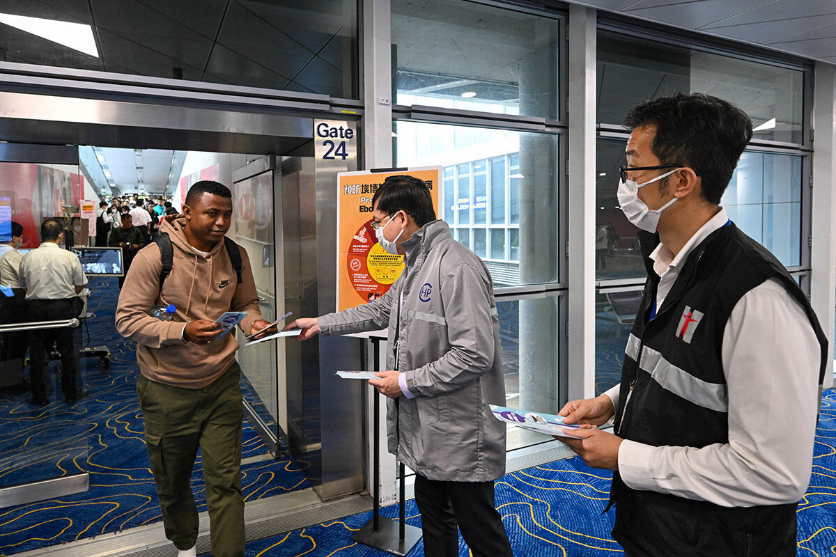 衞生防護中心傳染病處主任歐家榮(中)在機場向非洲抵港航班旅客派發伊波拉健康宣傳資料。(政府新聞處)