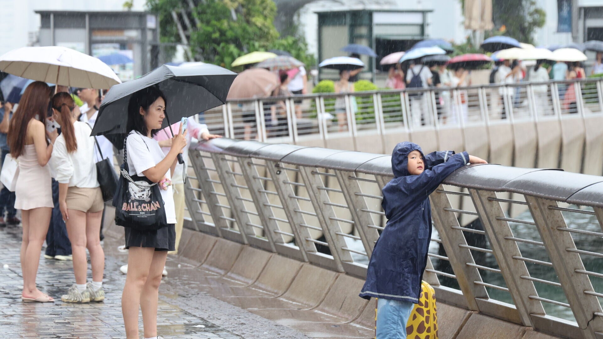 雨勢頗大，仍有不少遊客在維港海濱拍照打卡。（中通社）