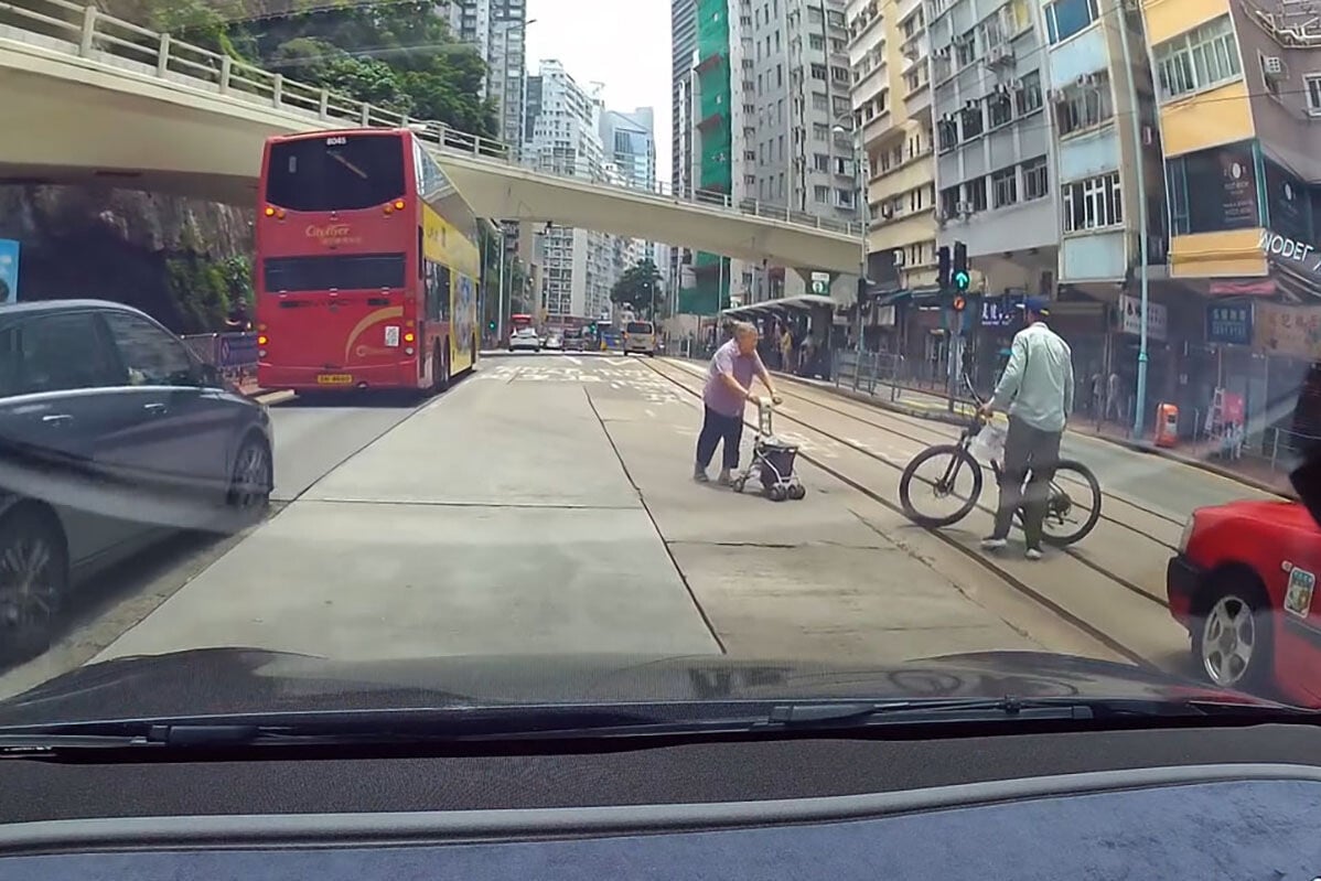 英皇道有一名推着四輪助行車的婆婆呆站路中,路過的南亞裔男子見狀把單車「閘停」的士,協助她安全離開馬路範圍。(網上影片截圖)
