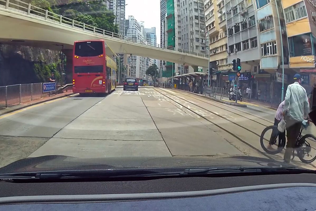 英皇道有一名推着四輪助行車的婆婆呆站路中,路過的南亞裔男子見狀把單車「閘停」的士,協助她安全離開馬路範圍。(網上影片截圖)