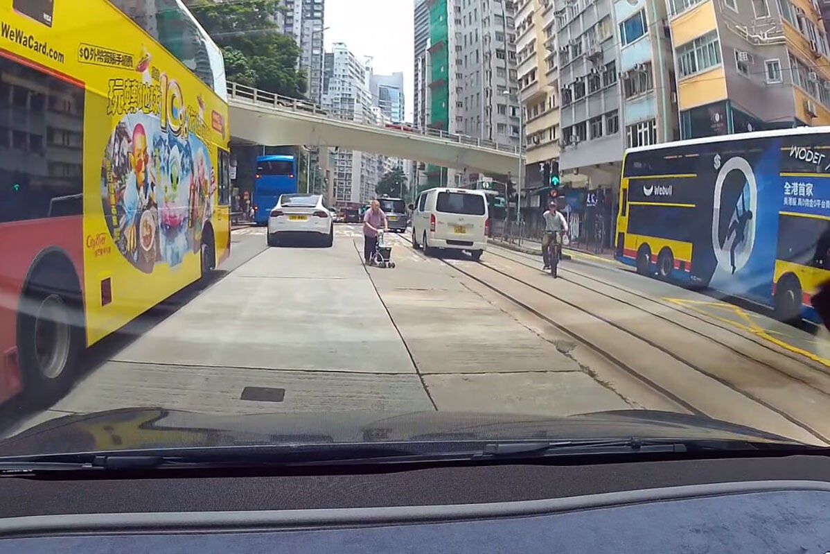 英皇道有一名推着四輪助行車的婆婆呆站路中,路過的南亞裔男子見狀把單車「閘停」的士,協助她安全離開馬路範圍。(網上影片截圖)