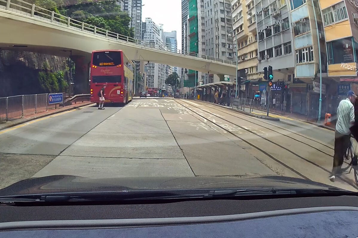 英皇道有一名推着四輪助行車的婆婆呆站路中,路過的南亞裔男子見狀把單車「閘停」的士,協助她安全離開馬路範圍。(網上影片截圖)