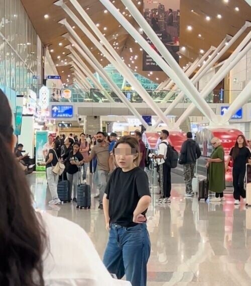 女子赤腳站在機場大廳中央,一手舉高,另一手叉腰。(X)