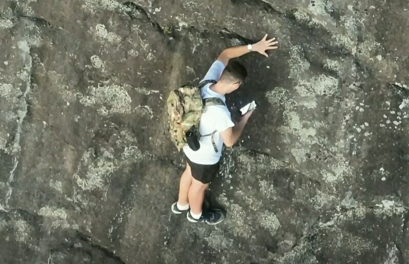 男子被迫單手抓著岩壁凸起處維持平衡,以騰出另一隻手拿出手機撥打911報案。(FB)