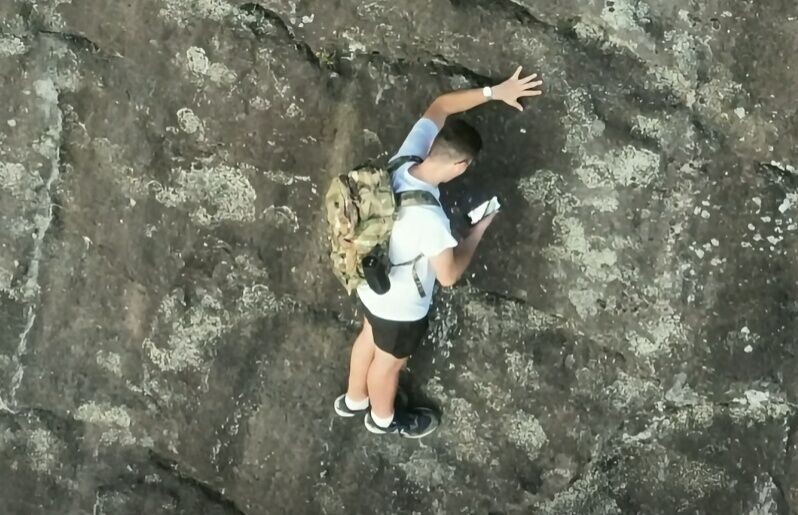 男子被迫單手抓著岩壁凸起處維持平衡,以騰出另一隻手拿出手機撥打911報案。(FB)