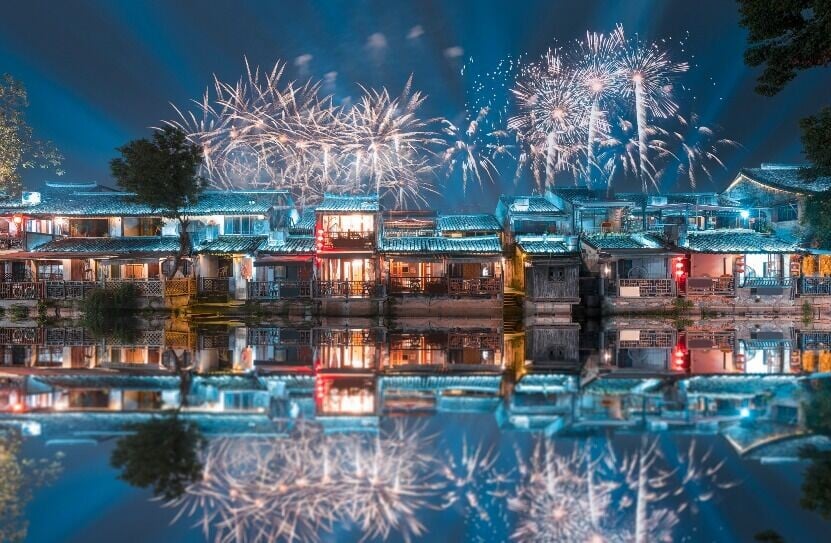 西塘古鎮,煙花在河面上方綻放,璀璨光點與兩岸燈火一同倒映水中,十分唯美。(圖片來源:視覺中國)