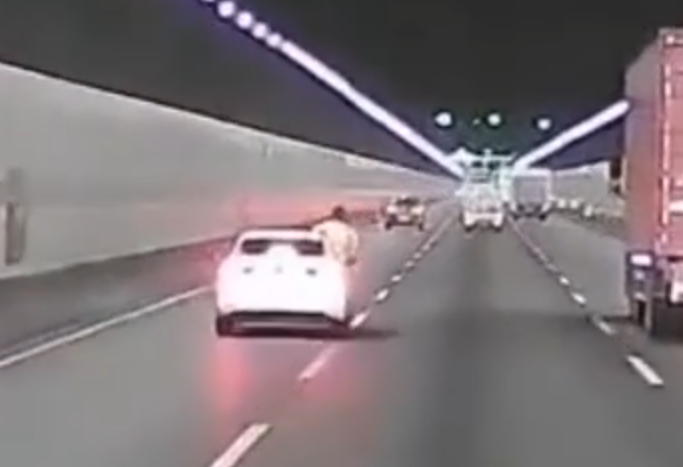 浙江錢江隧道一輛私家車在隧道內行駛期間,副駕駛座一名女子突然爬出車窗,站上車頂後突跳下,鄰線後方一輛大型貨車緊急避讓。(影片截圖)
