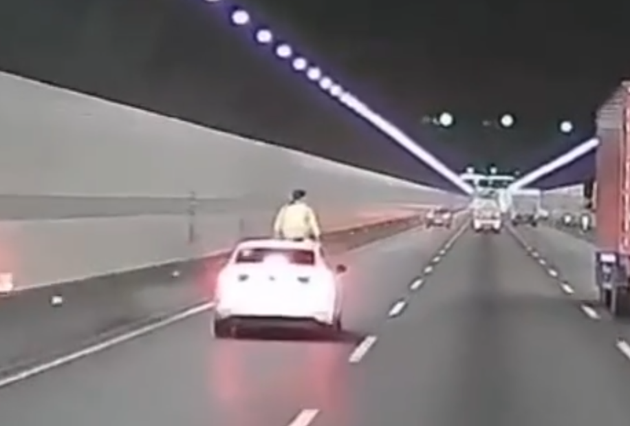 浙江錢江隧道一輛私家車在隧道內行駛期間,副駕駛座一名女子突然爬出車窗,站上車頂後突跳下,鄰線後方一輛大型貨車緊急避讓。(影片截圖)