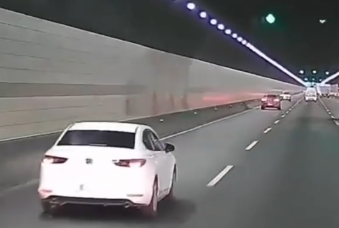 浙江錢江隧道一輛私家車在隧道內行駛期間,副駕駛座一名女子突然爬出車窗,站上車頂後突跳下,鄰線後方一輛大型貨車緊急避讓。(影片截圖)