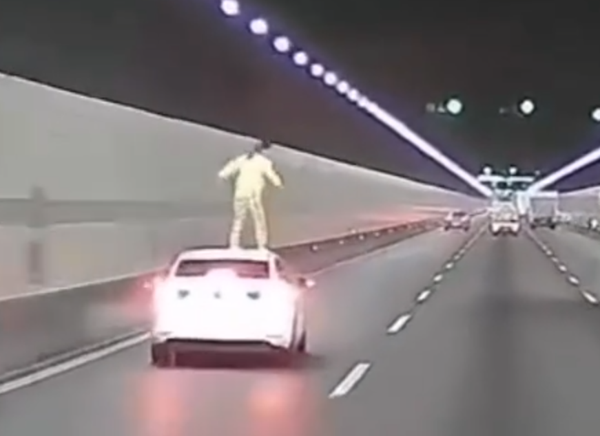 浙江錢江隧道一輛私家車在隧道內行駛期間,副駕駛座一名女子突然爬出車窗,站上車頂後突跳下,鄰線後方一輛大型貨車緊急避讓。(影片截圖)