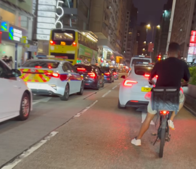 油麻地一名疑是外賣員的非華裔男子駕駛電動單車沿快線行駛,中線有一輛警車,慢線亦有另一名疑是外賣員的男子駕駛電動單車。(「車cam L(香港群組)」fb)
