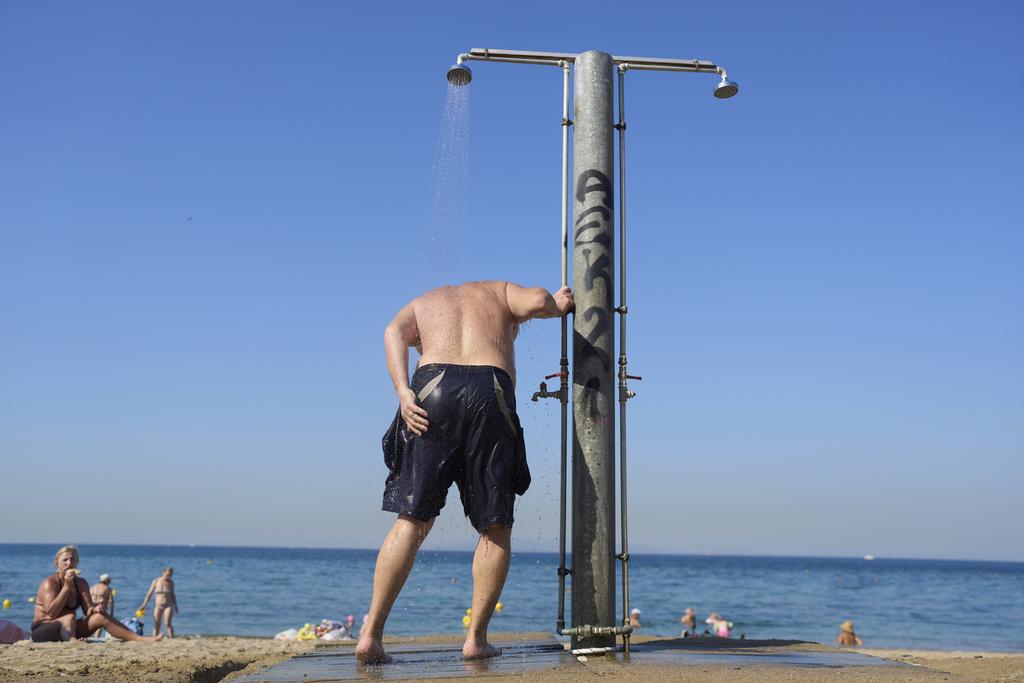 希臘雅典附近一處海灘,一名男子淋水降溫。(美聯社)