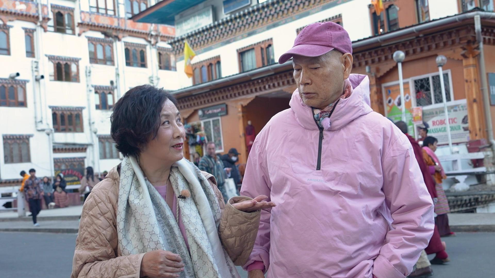 二人在不丹旅遊達人帶領下閒逛諾辛蘭大道,並購買節慶才發售的彩票。