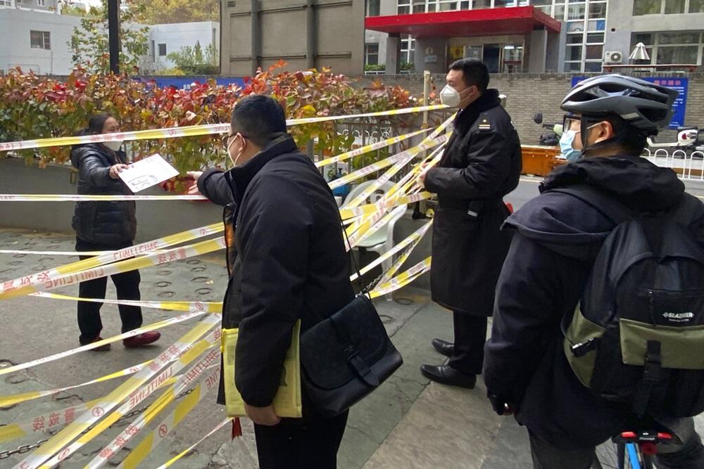 內地疫情進一步擴大，過去一日公布多2.6萬宗本土個案。圖示一名北京婦人向封控區市民傳遞信件。(美聯社)