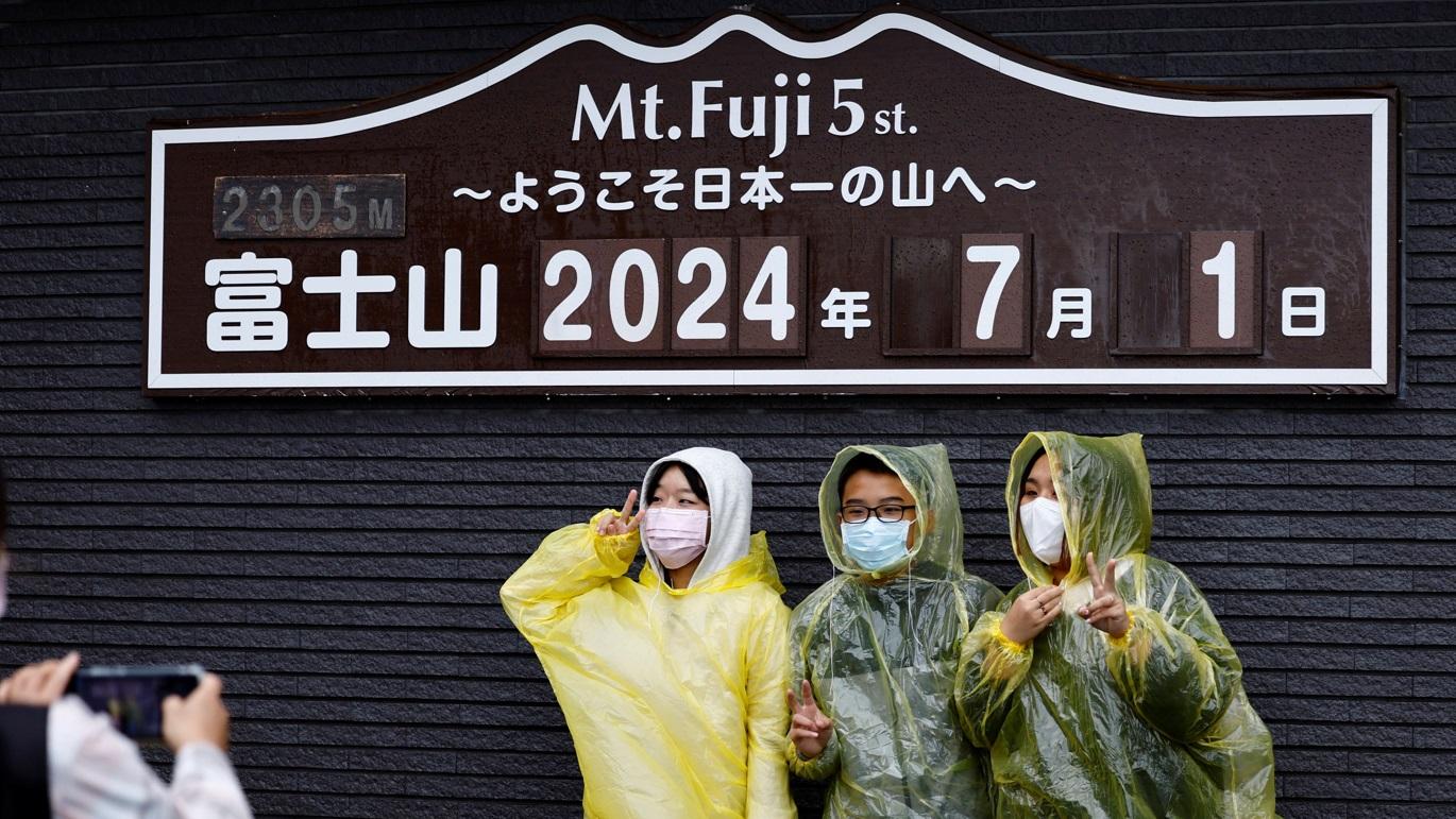 民眾在富士山五合目的標誌前冒雨打卡。(路透社)