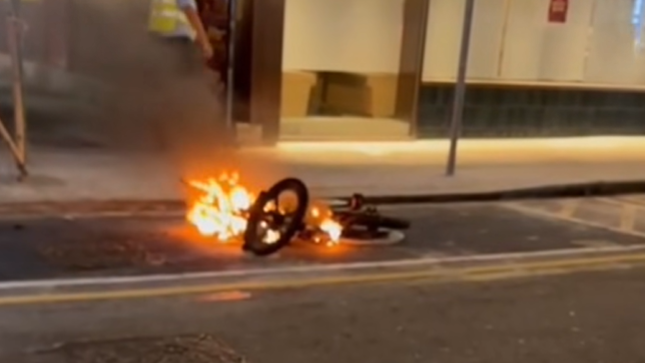倒在馬路邊的電動單車火光熊熊。(網上影片截圖)